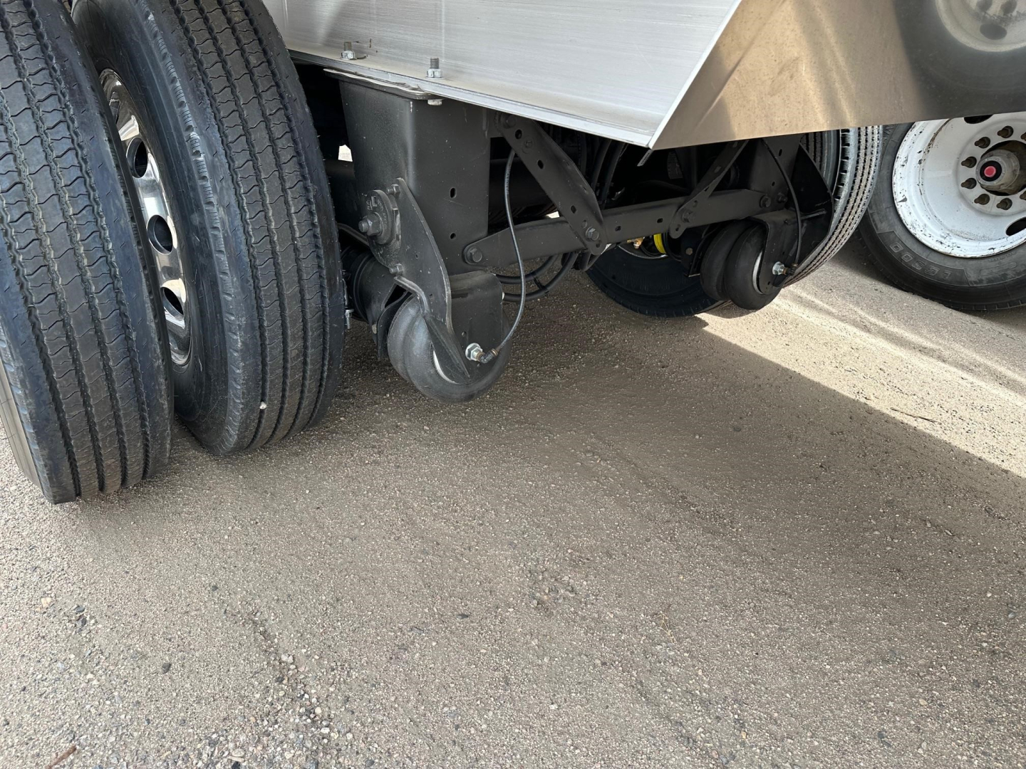 Trailer wheel hub and suspension undercarriage with dual rear tires and a caster wheel; aluminum end dump trailer side visible.