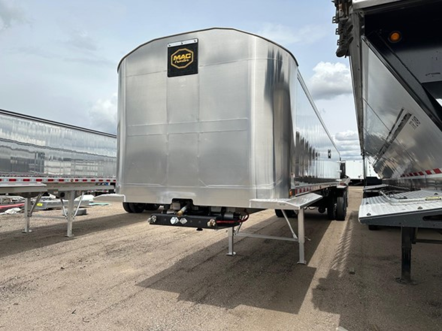 Mac Western Light Weight Alum End Dump trailer showing silver aluminum cargo body with a black Mac logo plate, rear underride bumper, and landing legs visible.