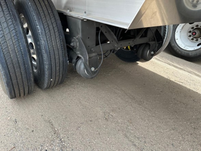 Trailer undercarriage showing suspension components, wheel hubs, and a caster trailer axle with dual tires and a leaf spring. Technical label not legible.