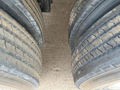 Trailer wheel pair with dual tires showing tread details and gravel surface between axles.