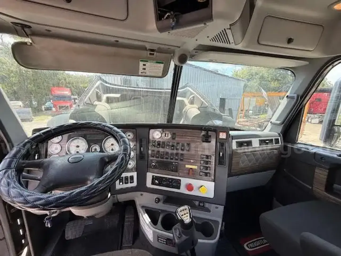 Cab interior of a 2015 Freightliner Coronado day cab showing steering wheel, instrument cluster, gear shifter, and dashboard controls.