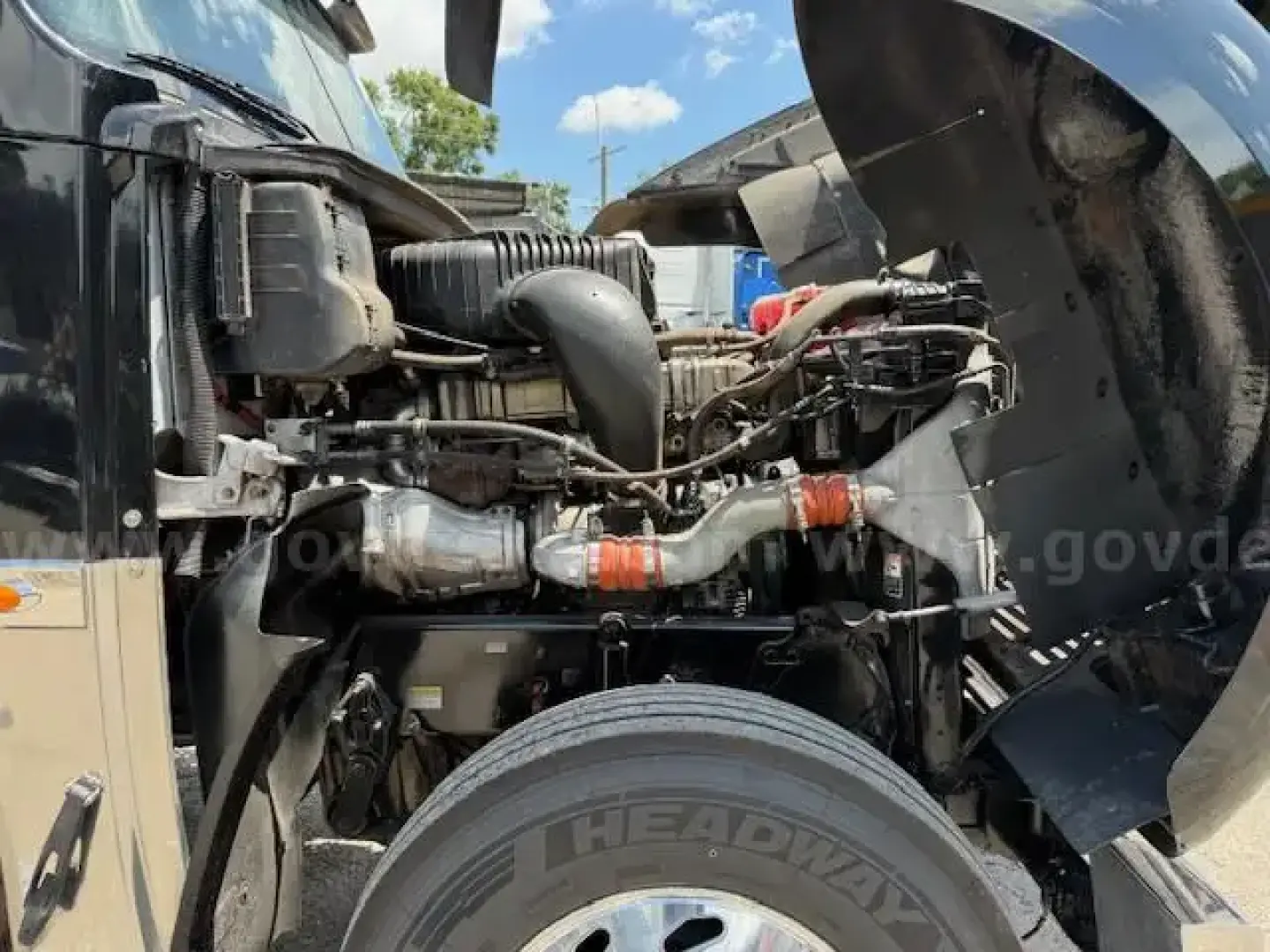 Front engine bay of a Freightliner Coronado day cab showing engine components, hoses, and air intake; partial cab and wheel visible.