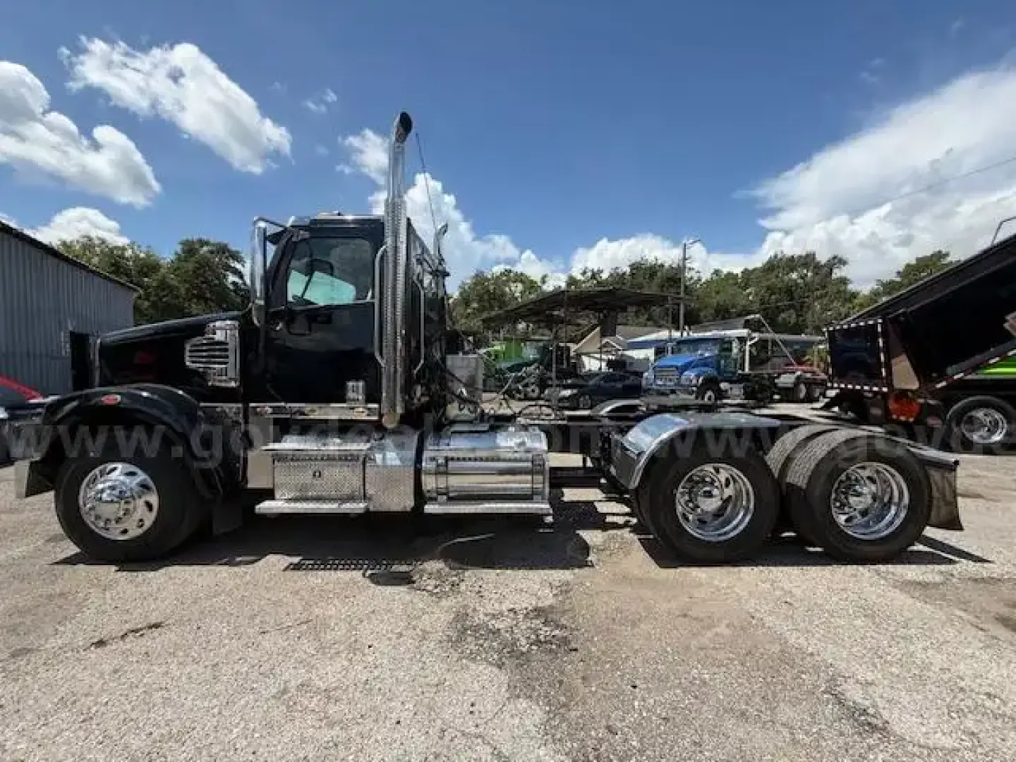 Freightliner Coronado day cab tractor seen in side profile with chrome fuel tanks and dual rear axles.
