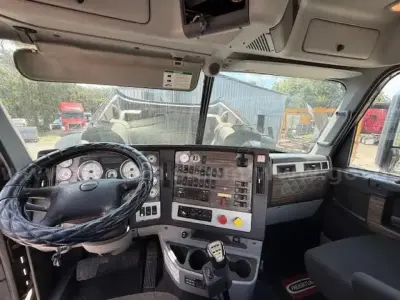 Cab interior of a 2015 Freightliner Coronado day cab showing steering wheel, instrument cluster, gear shifter, and dashboard controls.