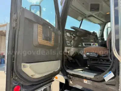 Truck cab interior with open driver door showing steering wheel and dashboard; Freightliner Coronado cab entry; VIN plate not visible.