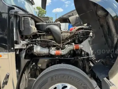 Front engine bay of a Freightliner Coronado day cab showing engine components, hoses, and air intake; partial cab and wheel visible.