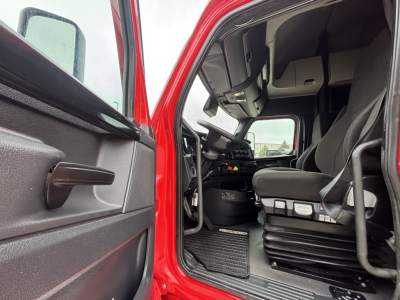 Truck cab interior view from open driver door showing steering wheel, dashboard, and seat in Freightliner PT126064ST cab.