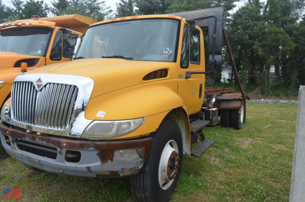 2003 International DuraStar 4300 roll-off truck in a yard showing front grille and cab with yellow paint and rust on bumper.
