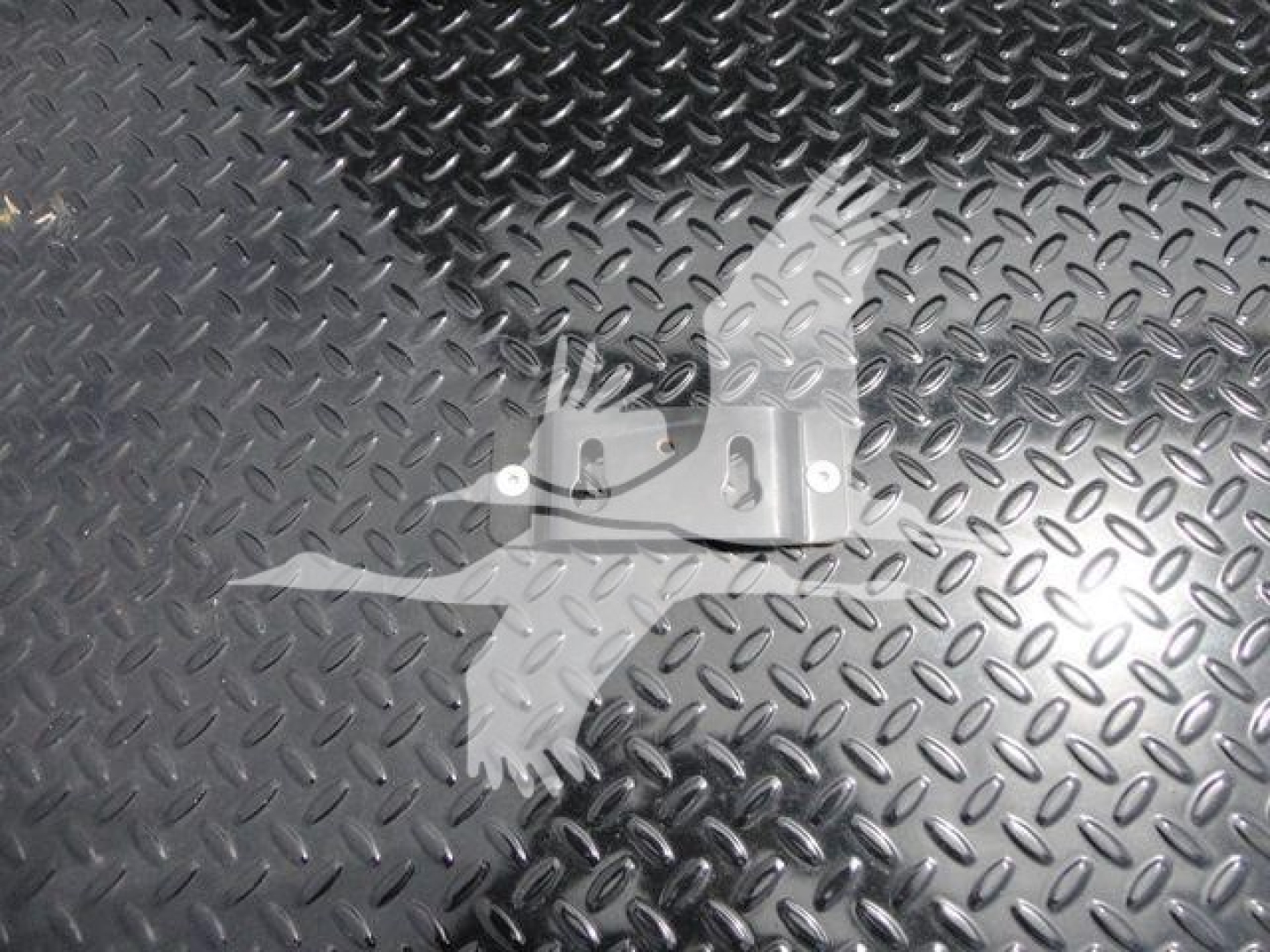 Metal diamond-plate surface with a small metal mounting bracket in foreground.