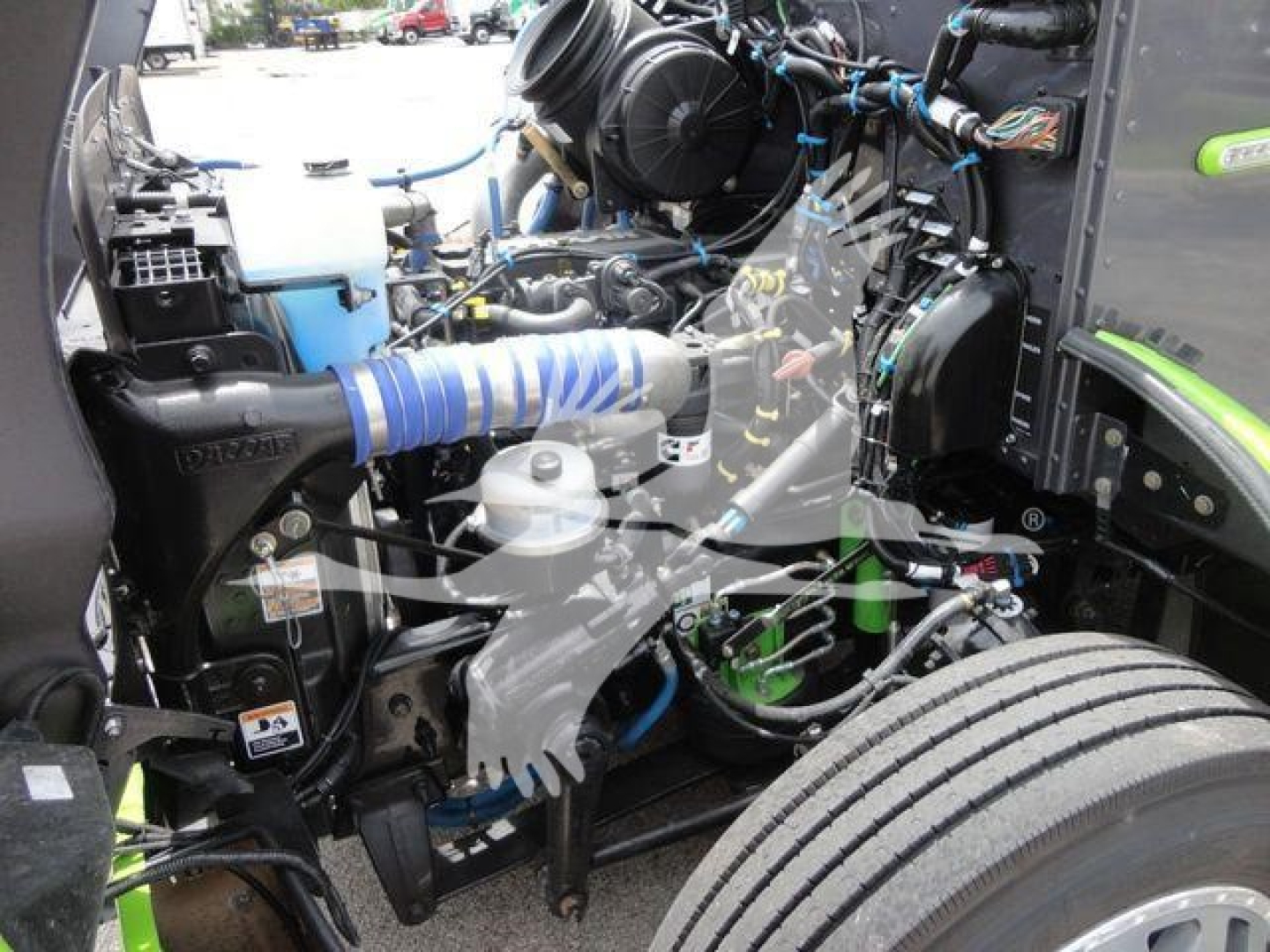 Peterbilt engine bay with blue intercooler hose and various hoses, wiring, and components visible; front wheel and fender in view.