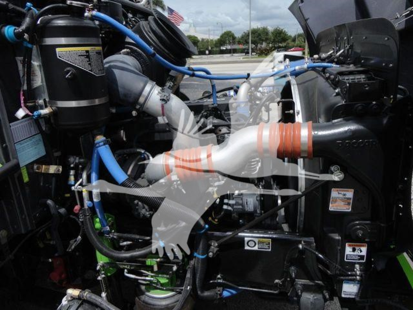 Trucks engine bay view showing blue and black hoses, exhaust components, and various labels in engine area.