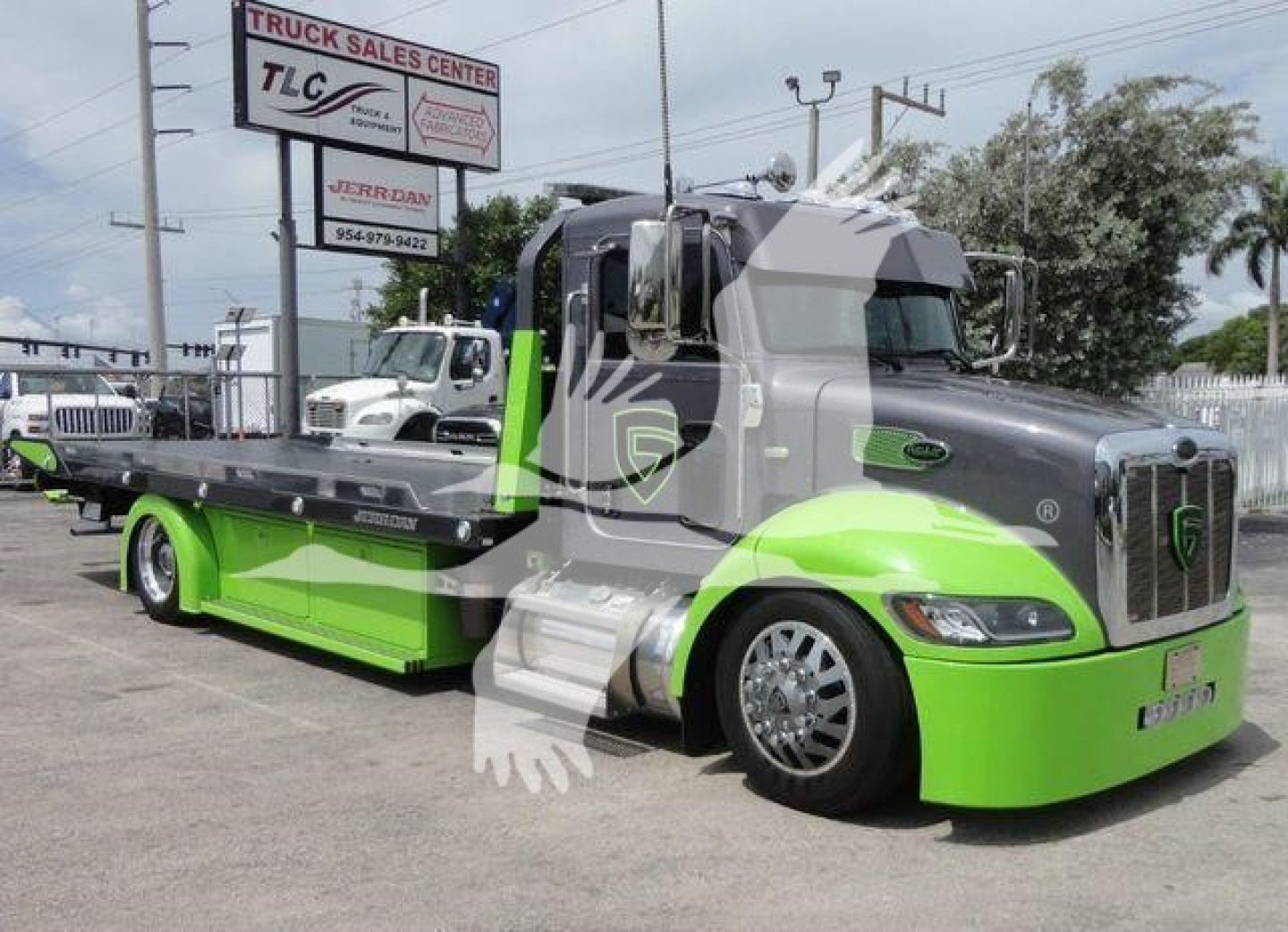 Peterbilt 337 tow truck with lime green lower cab and gray upper cab, rollback bed, dealership sign in background.