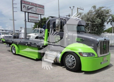 Peterbilt 337 tow truck with lime green lower cab and gray upper cab, rollback bed, dealership sign in background.