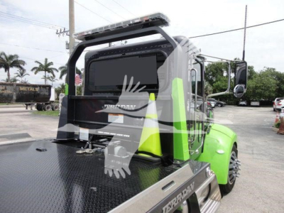2020 Peterbilt 337 rollback truck rear/right side showing neon-green cab and diamond plate flatbed with warning cones and rear window.