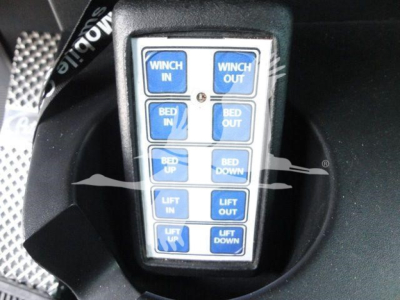 Truck control pendant showing buttons labeled Winch In, Winch Out, Bed In, Bed Out, Bed Up, Bed Down, Lift In, Lift Out, Lift Up, Lift Down.