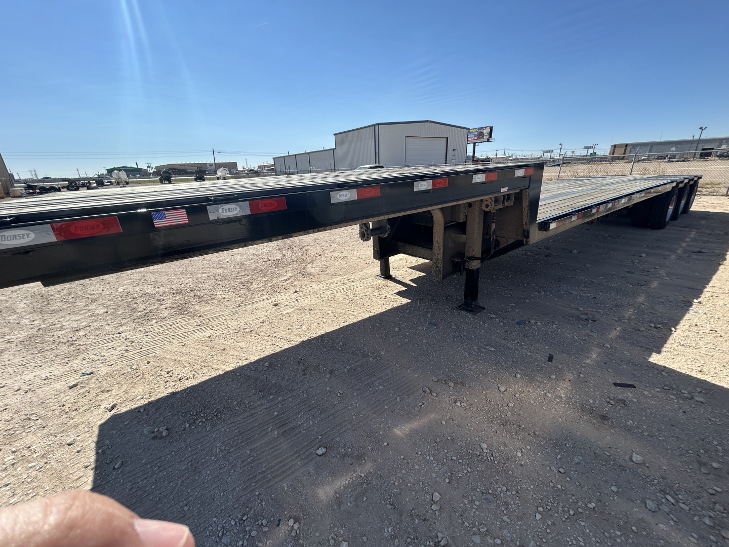 Trailer side view showing long flatbed with drop deck trailer support legs, with stock and yard in background.