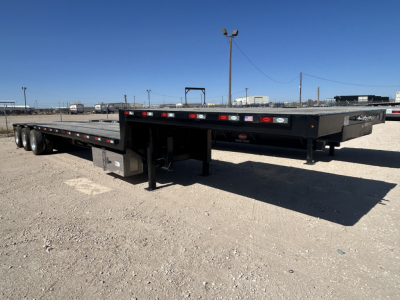 Trailer showing flatbed with dual rear axles and drop deck, black metal frame, with stakes and deck supports visible.