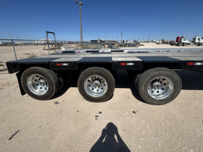 Trailer side view showing three axles with aluminum wheels and a flatbed deck. No legible labels visible on the side.