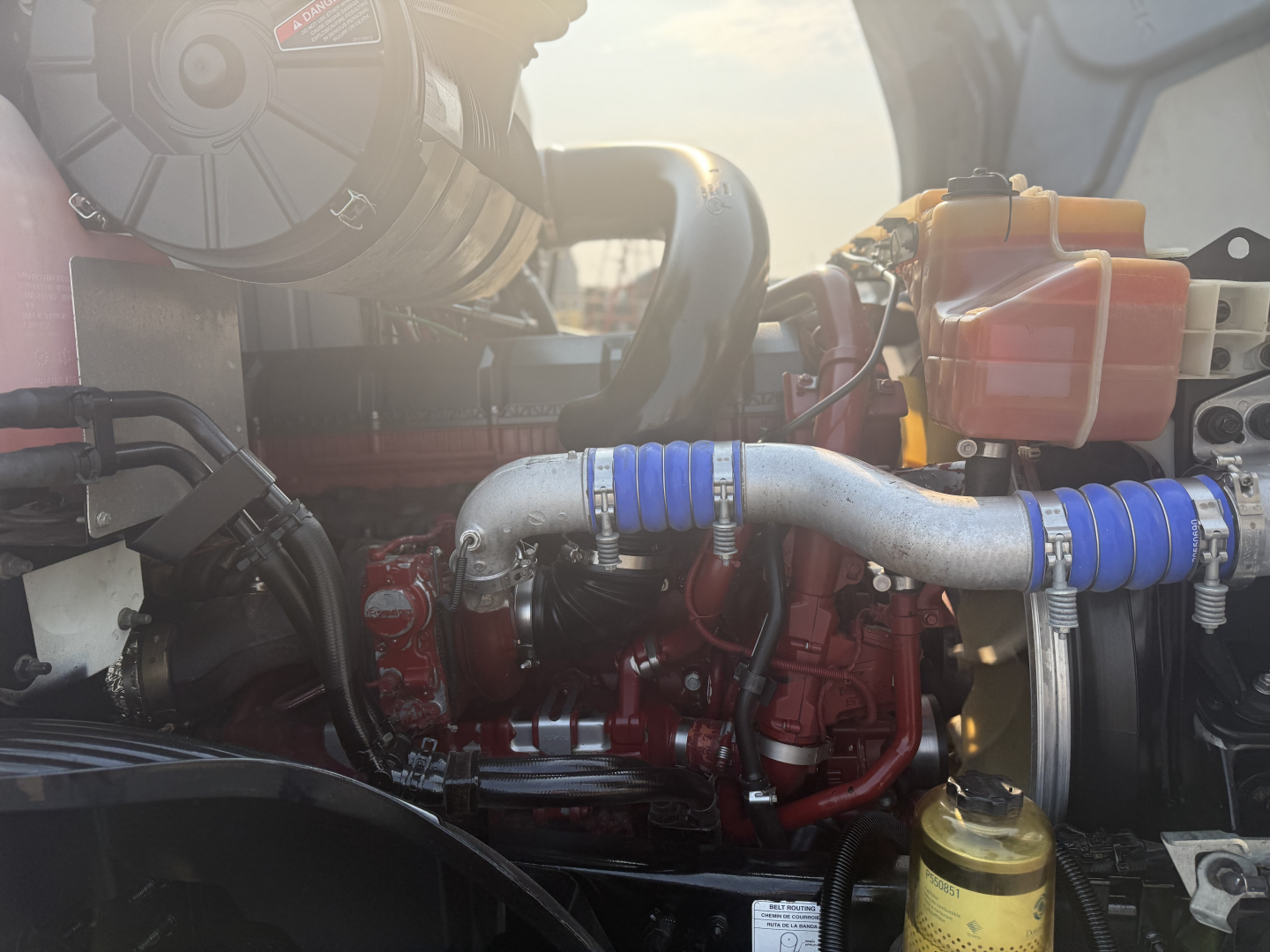 Engine bay of a 2020 Mack Anthem daycab showing turbo hoses, coolant reservoir, and engine components with blue silicone hoses and red engine block.