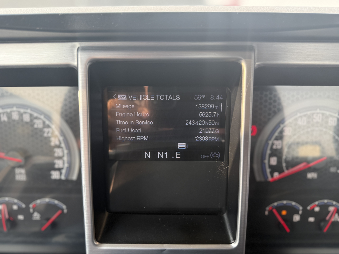 Dashboard display showing vehicle totals: mileage 138,929 mi; engine hours 1657.5?; time in service 243d 20h 56m; fuel used 2197 gal; highest RPM 2300; N N1 . E on screen.
