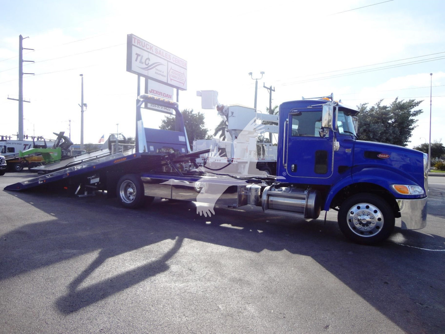 Blue 2022 Peterbilt 337 rollback wrecker chassis with black flatbed in a dealership lot showing long raised bed and chrome wheels.