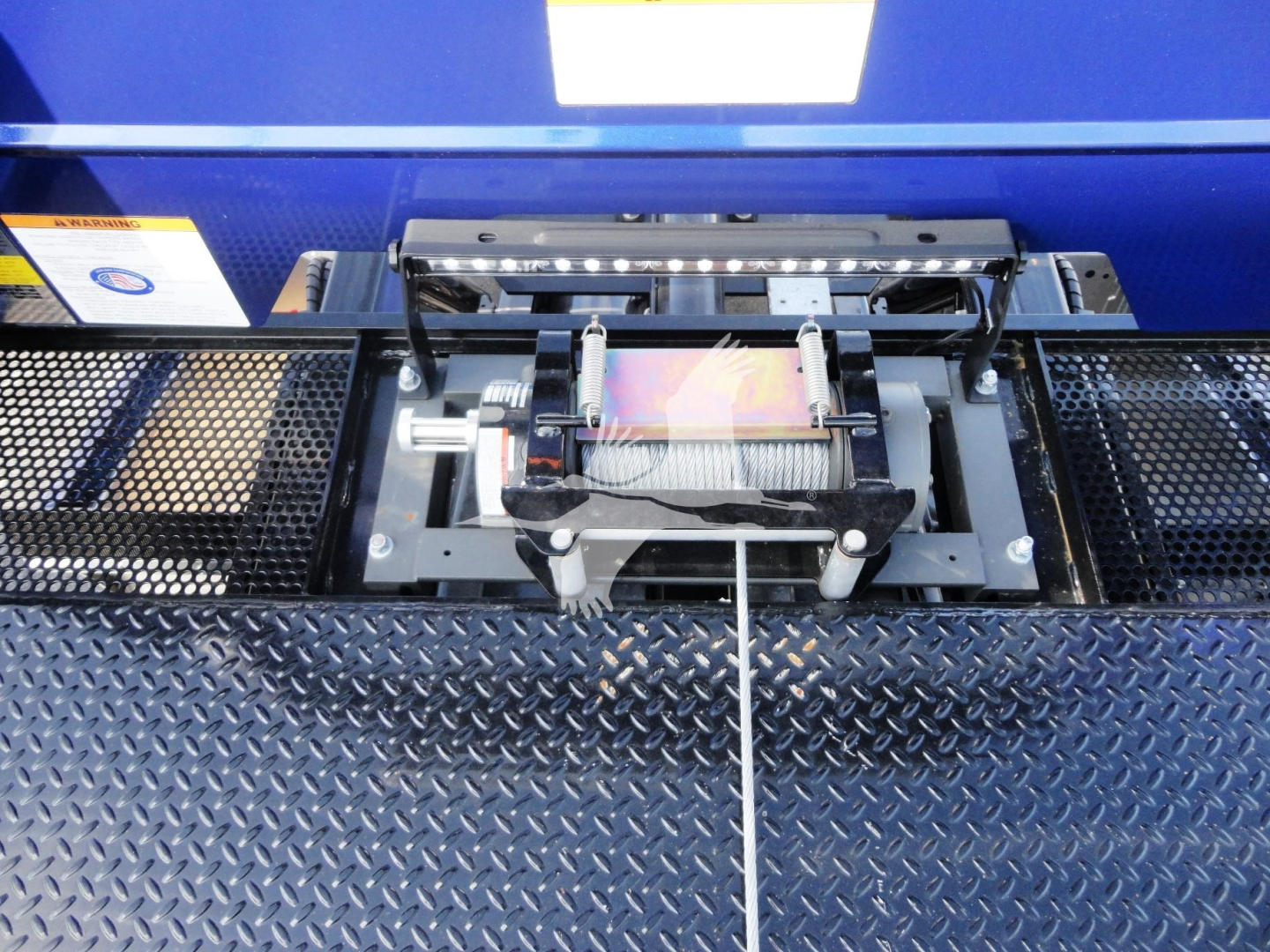 Truck bed winch assembly on a Peterbilt 337 rollback truck, visible winch drum, cable, and mounting hardware in a diamond plate bed.