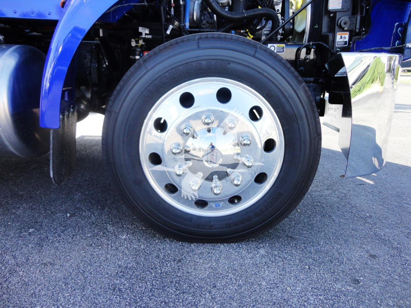 Peterbilt 337 front wheel showing polished steel hub and black tire, part of blue truck body.