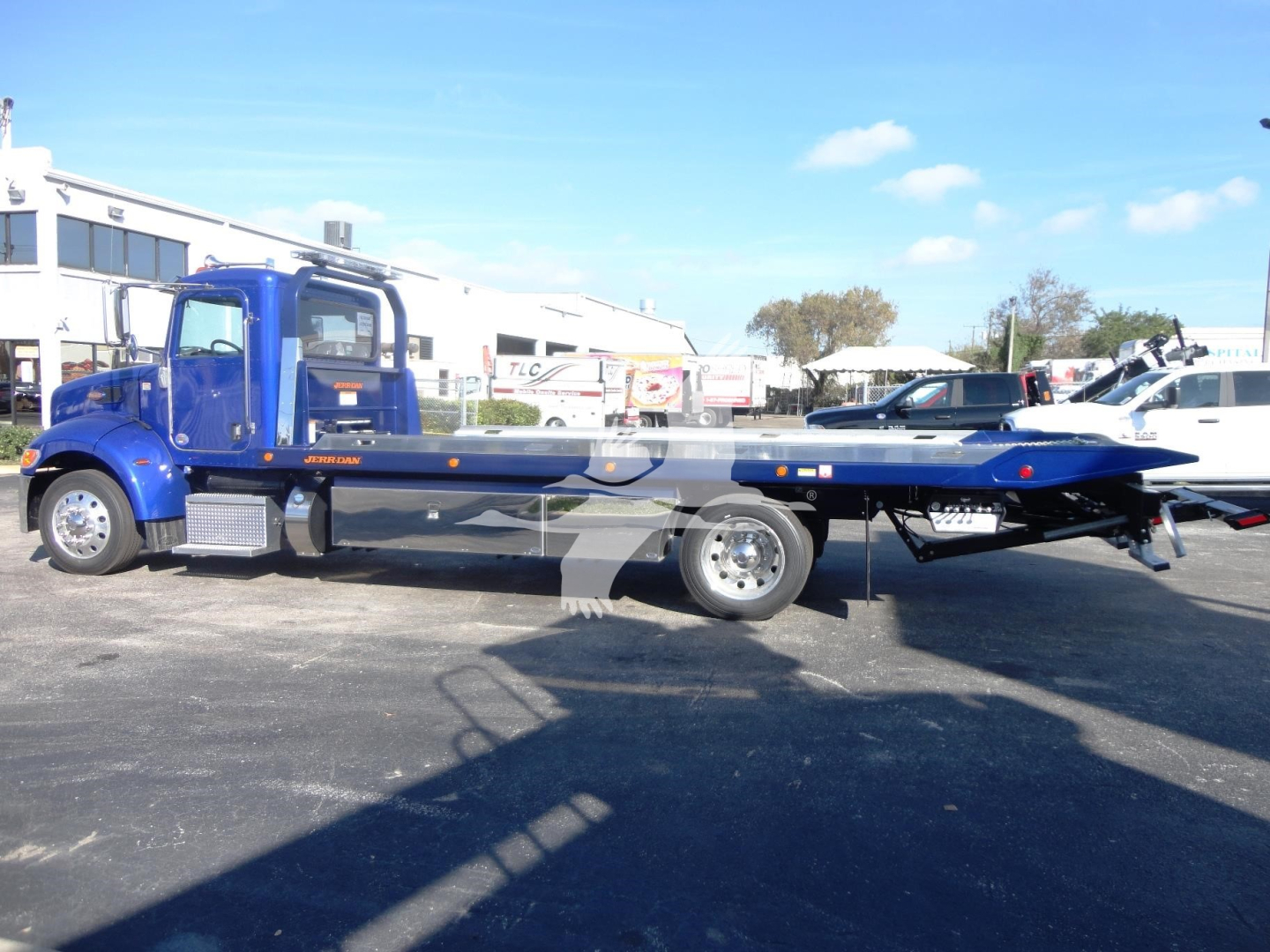 Blue Peterbilt 337 rollback tow truck with flatbed, side view showing cab and long bed.