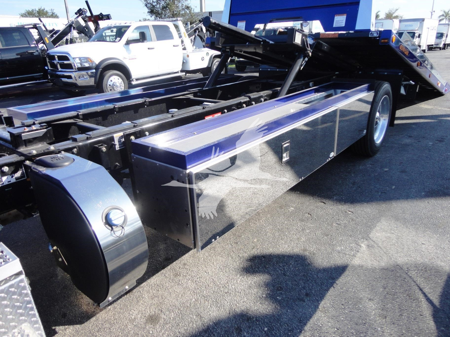 Peterbilt 337 rollback truck chassis with shiny metal toolbox and hydraulic bed, blue frame, side view showing fuel tank and wheel.
