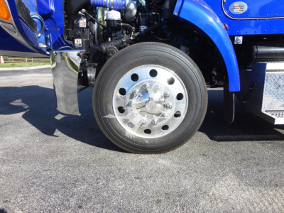 Peterbilt 337 front wheel and blue fender showing polished aluminum wheel and hubcap with side steps and engine bay components visible