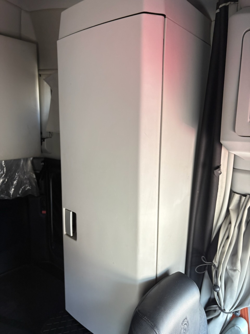Kenworth T680 truck interior showing a tall vertical cabinet/box with a small latch on its front, cables and a curtain nearby.