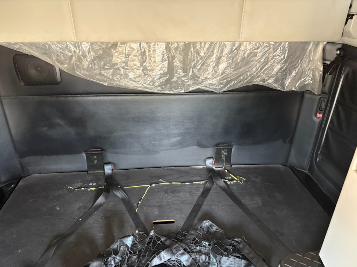 Kenworth T680 sleeper cab interior cargo area with folded rear seats and strap anchors, rear wall cover, and a plastic sheet at top.