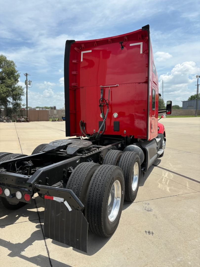 Kenworth T680 tractor rear undercarriage with triple rear axles and red sleeper cab; visible tires, mudflaps, and chassis; no text readable on stickers.
