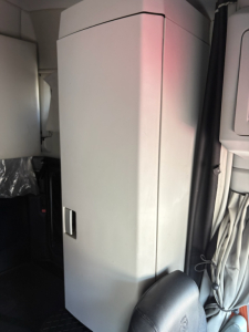 Kenworth T680 truck interior showing a tall vertical cabinet/box with a small latch on its front, cables and a curtain nearby.