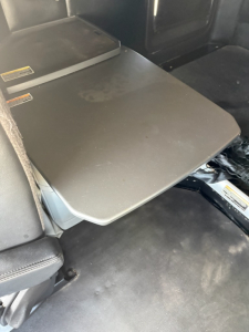 Table/desk folded in cargo area of a Kenworth T680 cab, with cargo area seating nearby; interior storage surface visible.