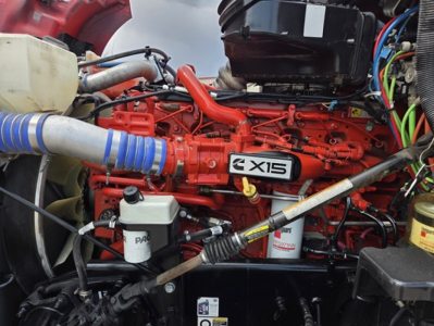 Kenworth T680 engine bay showing Cummins X15 engine badge and red engine block with hoses and fluid reservoirs.