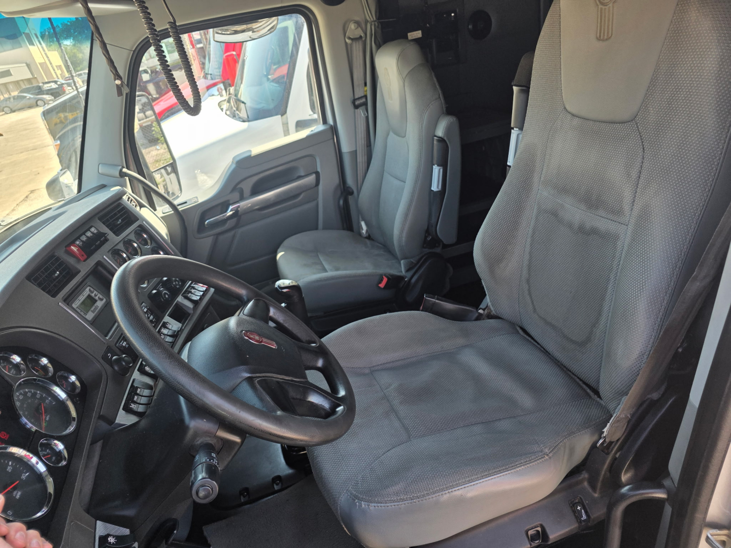 Kenworth T680 truck cabin interior showing steering wheel, driver's seat, and dashboard with gauges.