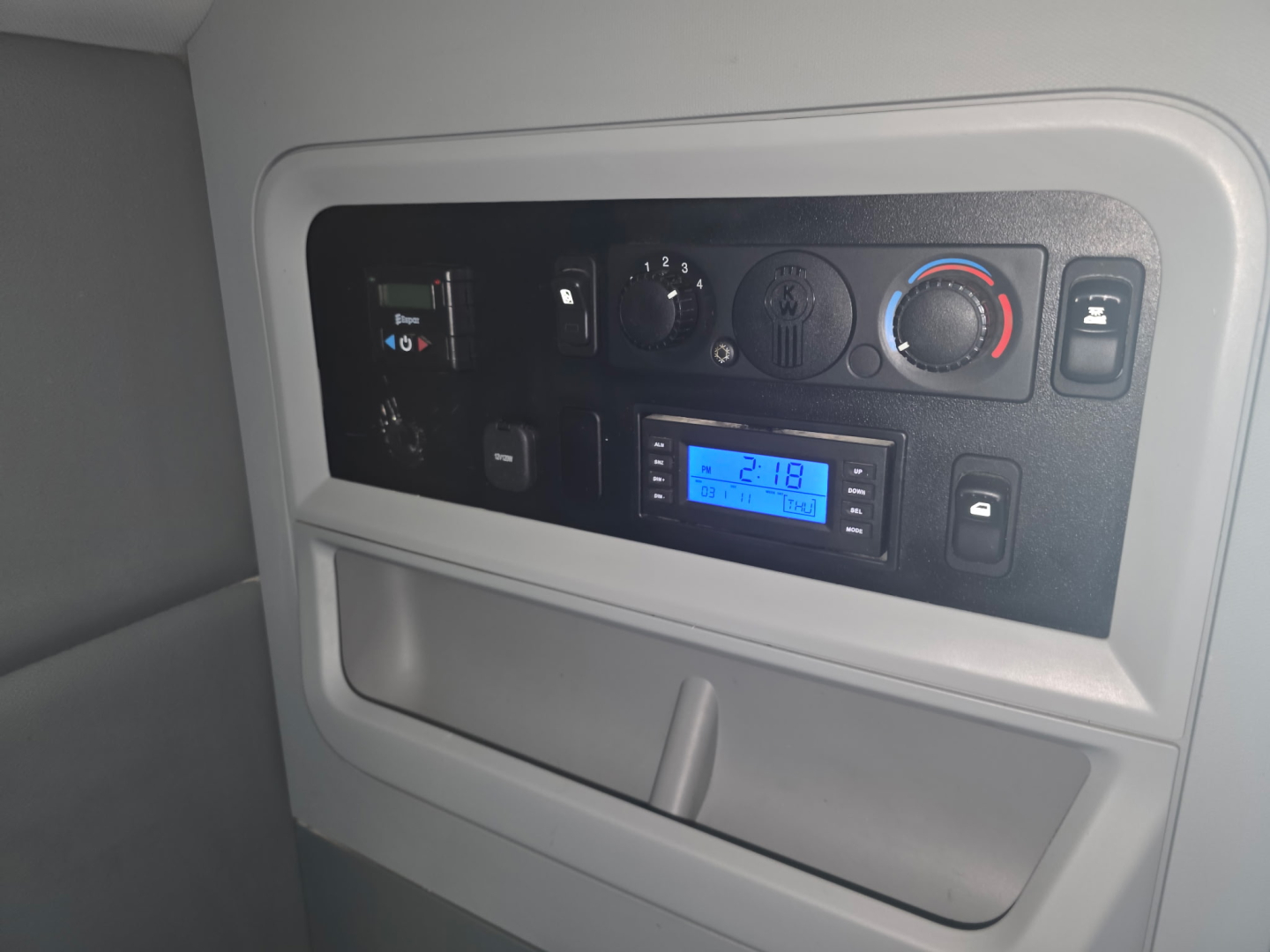 Dashboard area of a 2018 Kenworth T680 sleeper truck cab showing instrument cluster, climate controls, and a blue digital display along with various switches.