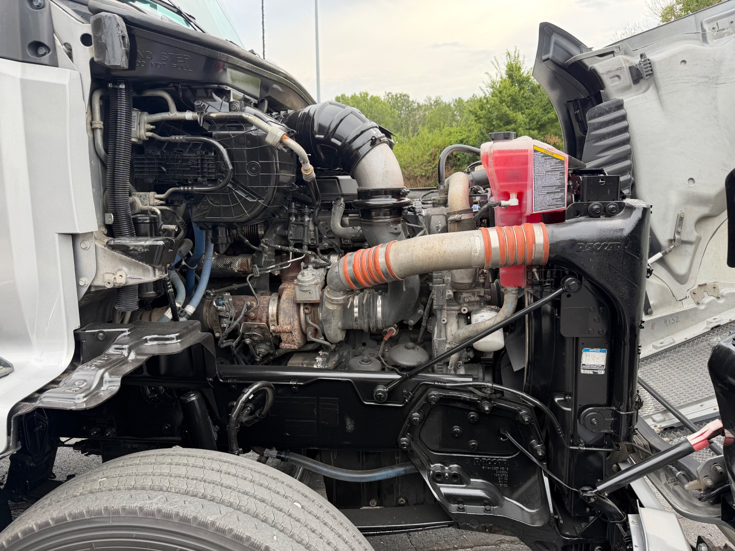 Kenworth T680 engine bay showing diesel engine components, air intake hose, radiator, and coolant reservoir.