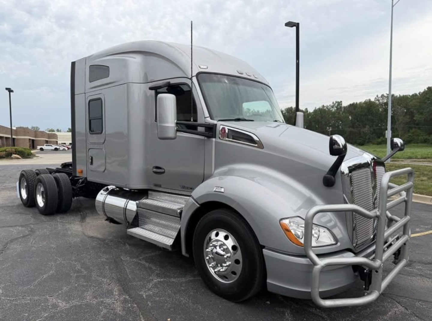 Kenworth T680 semi-truck in silver/gray with sleeper cab, front grille guard, dual rear axles, side steps, fuel tanks visible.