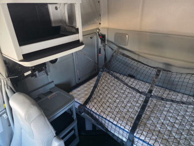 Kenworth T680 sleeper cab interior showing cargo area with a fold-down bunk and storage shelf; mesh cargo net and side panel visible.
