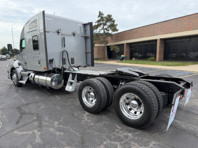 Kenworth T680 tractor sleeper cab side view showing dual rear wheels and chassis, gray exterior, fuel tanks, and rear mud flaps.