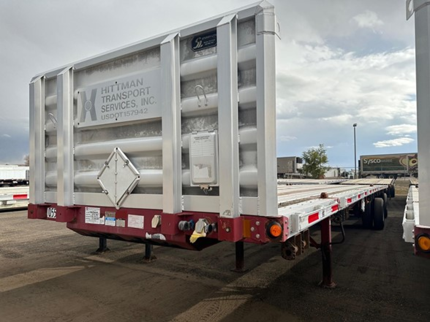 Flatbed trailer showing rear with Hitman Transport Services US DOT plate, tandem axles, and rear bumper lights.