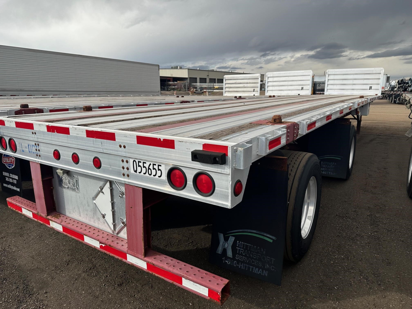 Flatbed trailer from rear-left view with aluminum deck, red-and-white reflective tape, taillights, and dual rear wheels; visible stock number 055655 and spare wheel area; Fontaine logo partially visible.