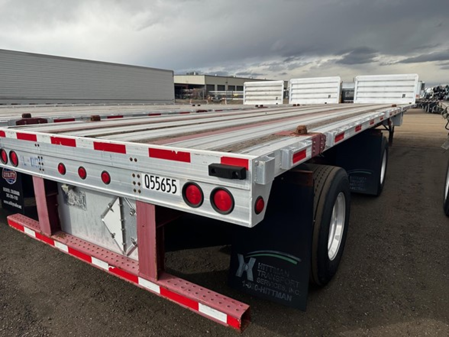 Flatbed trailer rear and side showing aluminum deck and red/white reflective tape with taillights and mudflaps.