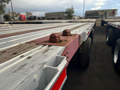 Flatbed trailer side with metal deck, red lugs, and dual axle wheels visible.