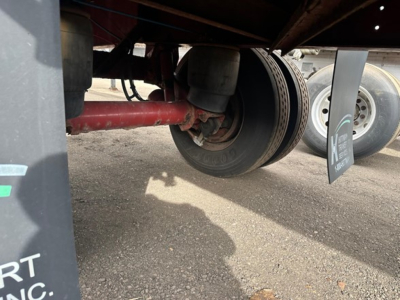Trailer axle and wheel assembly showing dual tires and red suspension component under Fontaine Infinity flatbed trailer