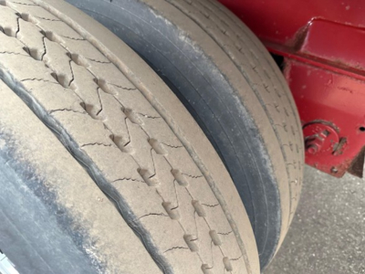 Trailer tire close-up showing tread and sidewall with chalky dust and wheel well; red trailer frame in background.