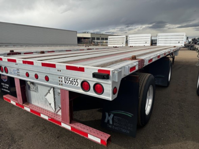 Flatbed trailer rear/right side showing aluminum deck, red and white reflective tape, taillights, mudflap, and stock number 055655 on rear bumper.