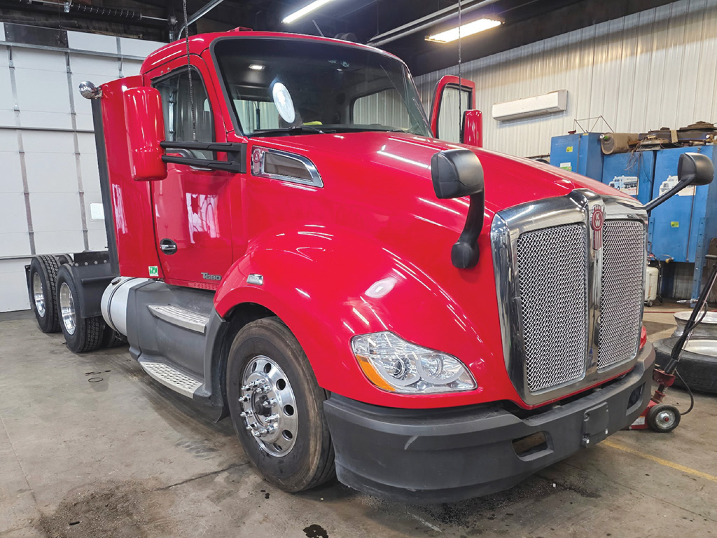 Kenworth T680 conventional daycab tractor in red, front left view in a shop with stock/VIN details not visible on the cab.